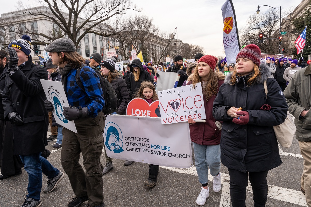 Young woman with Orthodox marchers holds up sign