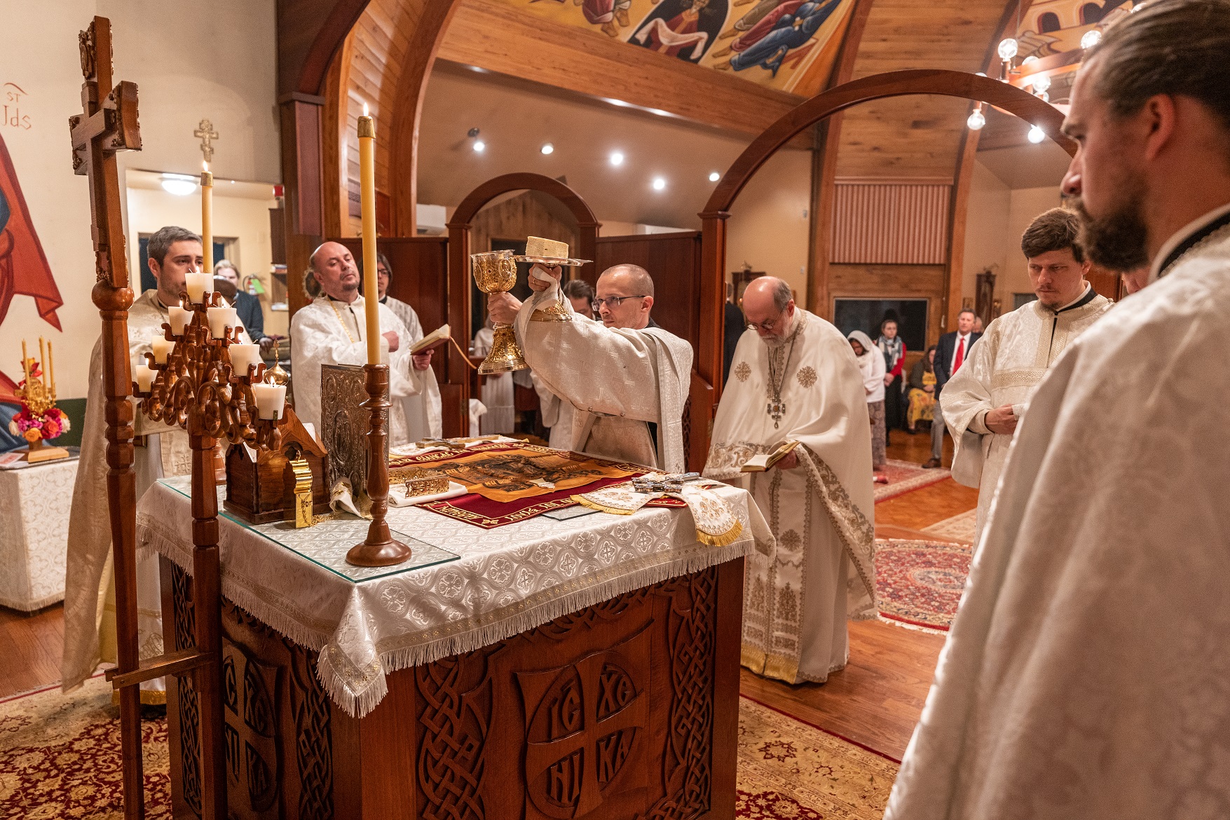 Fr Chad holds up paten and chalice during Pascha liturgy with clergy surrounding the altar