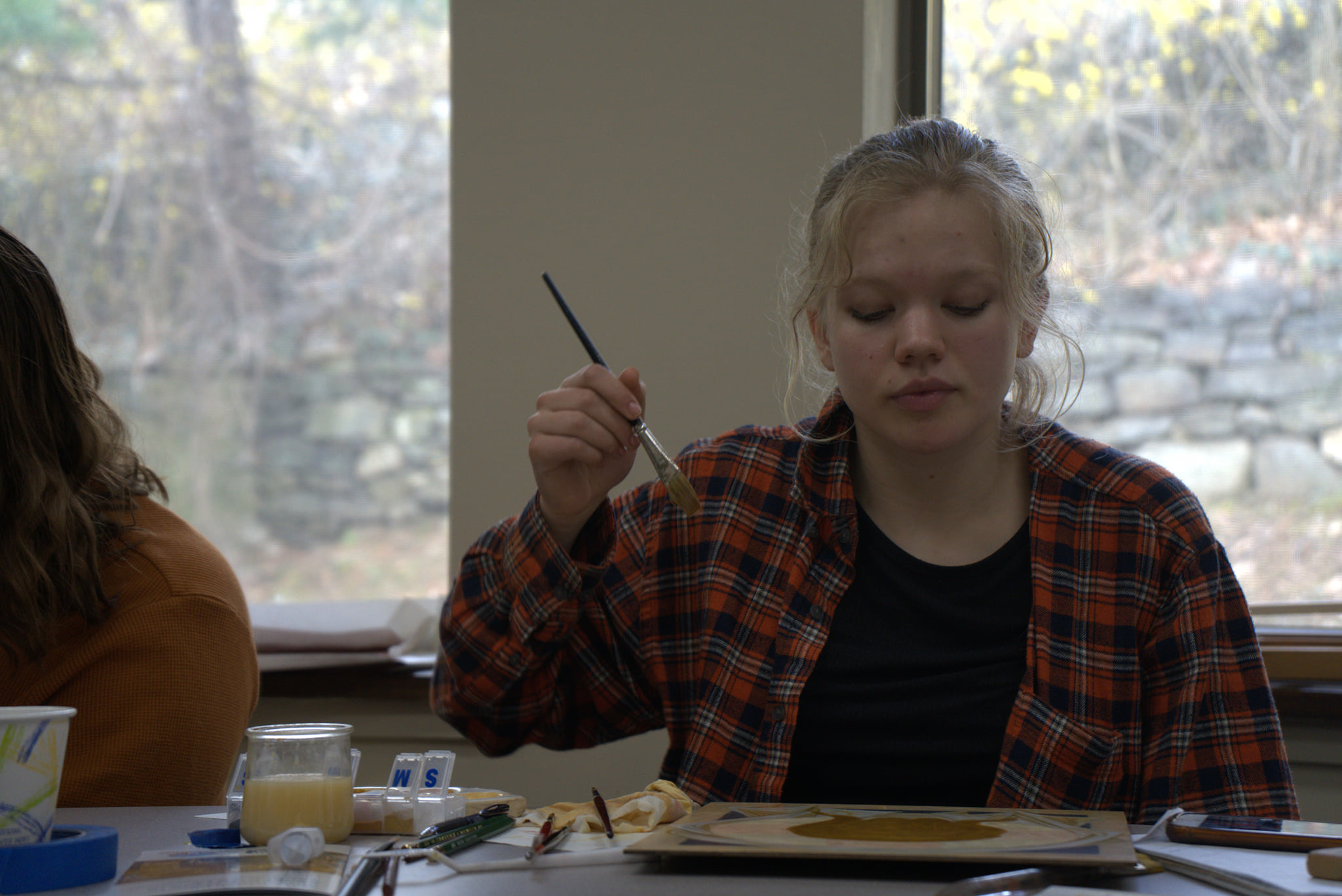 Workshop student holds up a brush as she examines her icon-in-progress
